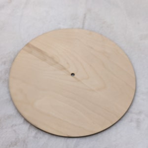 May include: A round, unfinished wooden disc with a small hole in the center. The light-colored wood has a natural grain pattern. This blank wooden circle is suitable for various craft projects.