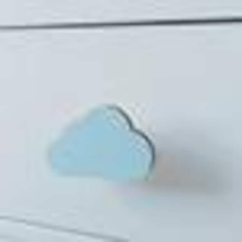 May include: A white chest of drawers with a light blue cloud-shaped handle. The handle is made of wood and has a simple design. The chest of drawers has a smooth, painted finish.