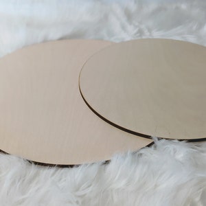 May include: Two round wooden discs, one slightly larger than the other, are stacked on top of each other. The discs are a light brown color and have a smooth, unfinished surface.