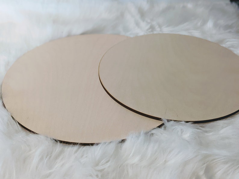 May include: Two round wooden discs, one slightly larger than the other, are stacked on top of each other. The discs are a light brown color and have a smooth, unfinished surface.