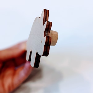 May include: A wooden cutout of a rhinoceros in a light brown color with a dark brown outline. The cutout is held in a hand.