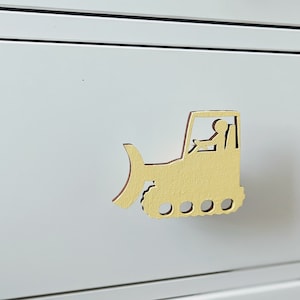 May include: Yellow wooden drawer pull shaped like a bulldozer with a driver in the cab.
