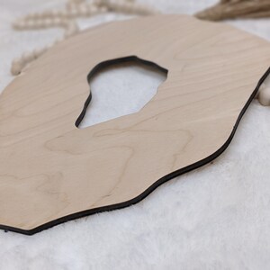 May include: A light brown wooden cutout in the shape of an agate with a hole in the center. The cutout has a dark brown border.