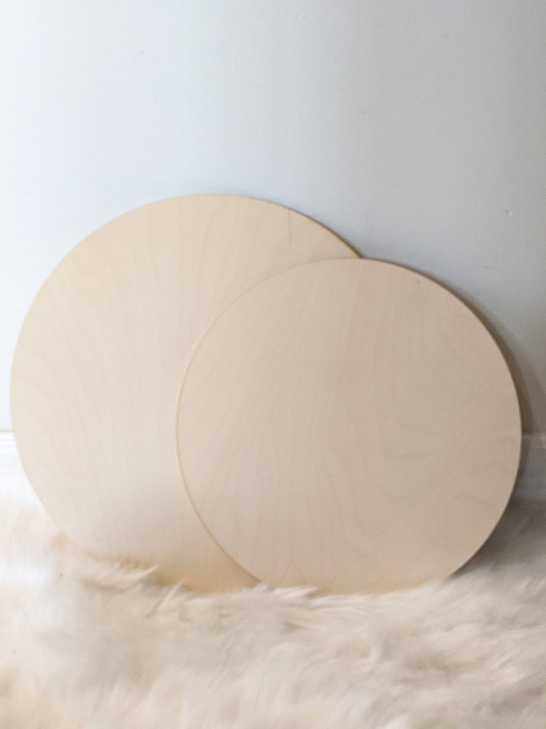 May include: Two unfinished wooden circles, one larger than the other, on a white fluffy surface.