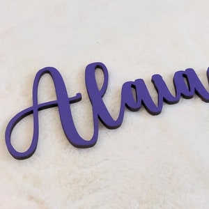 Peut inclure: Une plaque de nom en bois violet avec le nom "Alaina" écrit en cursive.