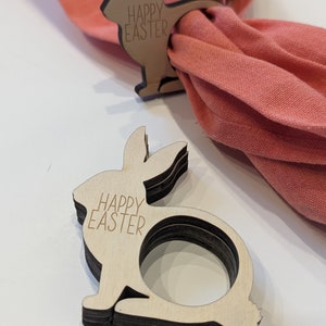 Op de afbeelding: Twee houten konijnen servetringen met de tekst "Happy Easter" erop gegraveerd. De ringen zijn op elkaar gestapeld.