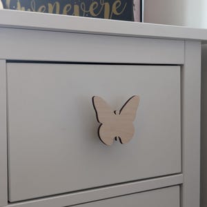 Peut inclure: Commode blanche avec une poignée de tiroir en forme de papillon en bois.