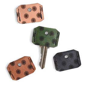 May include: Key covers in shades of tan, brown, green, and black, each with a floral pattern. One key is inserted into a green cover. The covers are made of leather and have a metal rivet for key insertion.