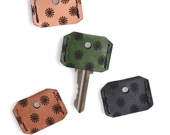 May include: Key covers in shades of tan, brown, green, and black, each with a floral pattern. One key is inserted into a green cover. The covers are made of leather and have a metal rivet for key insertion.