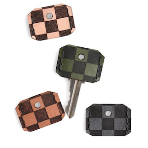 May include: Four keychains with a checkerboard pattern in various colors: light brown, dark brown, green, and gray. One keychain holds a silver key. Each keychain has a metal rivet.