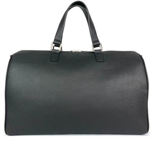 Puede incluir: Una bolsa de viaje de cuero negro con un solo asa superior y cierre de cremallera.