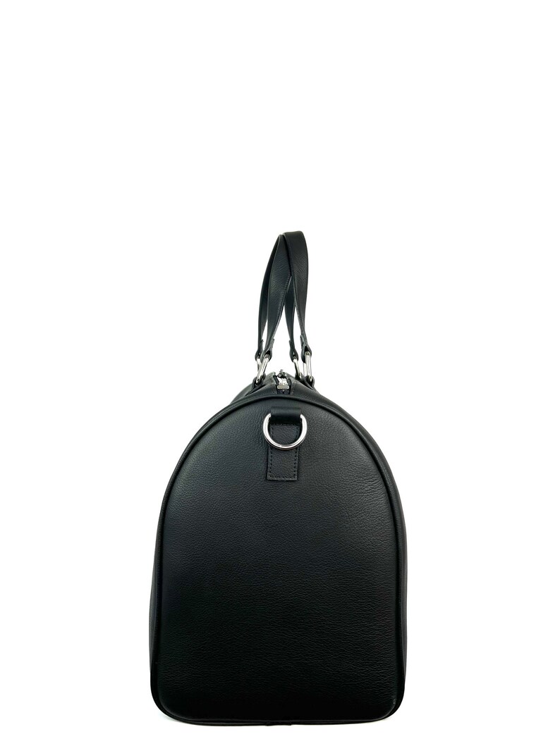 Puede incluir: Una bolsa de viaje de cuero negro con una cremallera plateada y un asa de anillo plateada.