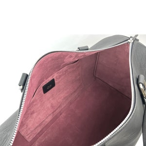 Puede incluir: Bolsa de viaje de cuero negro con cierre de cremallera y forro de tela rosa. La bolsa tiene un peque&ntilde;o bolsillo en el interior y el nombre de la marca "DMK" es visible.