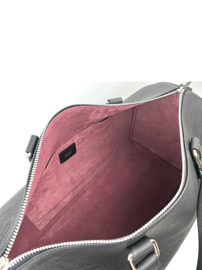 Puede incluir: Bolsa de viaje de cuero negro con cierre de cremallera y forro de tela rosa. La bolsa tiene un peque&ntilde;o bolsillo en el interior y el nombre de la marca "DMK" es visible.