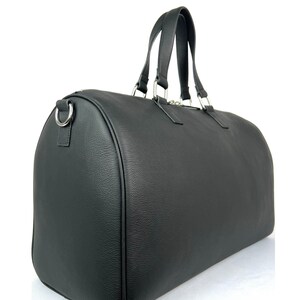 Puede incluir: Una bolsa de viaje de cuero negro con herrajes plateados y dos asas superiores.