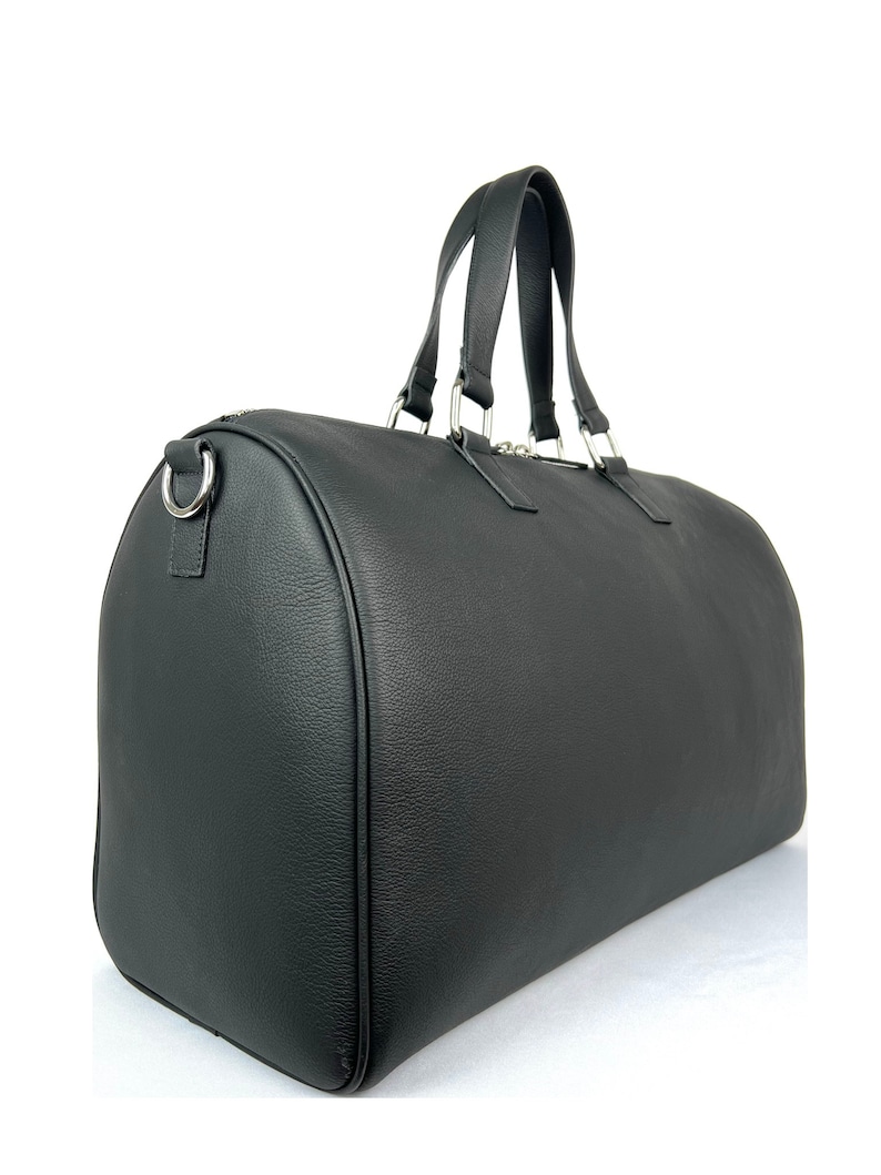 Puede incluir: Una bolsa de viaje de cuero negro con herrajes plateados y dos asas superiores.