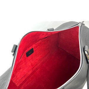 Puede incluir: Bolsa de viaje de cuero negro con forro interior rojo y cremallera plateada. La bolsa tiene un peque&ntilde;o bolsillo en el interior con la palabra "O.M.K." impresa en &eacute;l.