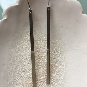May include: A pair of silver dangle earrings with long, thin, rectangular shapes.