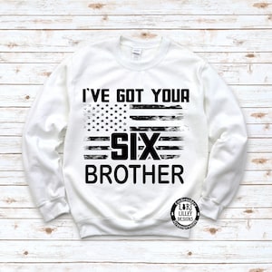 Può includere: Felpa bianca con un designo di bandiera americana in stile distressed nero e il testo "I've got your six brother".