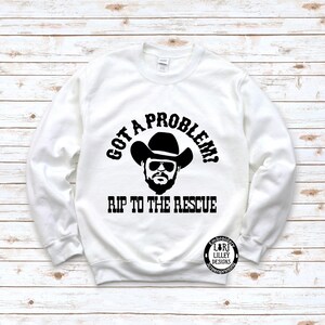 May include: White sweatshirt with black text that reads "Got a problem? Rip to the rescue". A black and white illustration of a man wearing a cowboy hat is above the text.