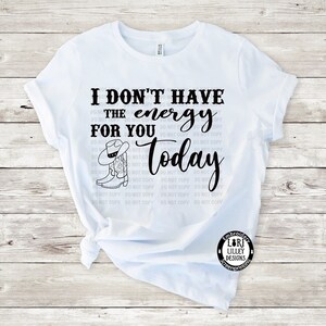 May include: White t-shirt with black text that reads "I don't have the energy for you today". The text is surrounded by a pattern of "Do Not Copy" in smaller font. A black and white illustration of a cowboy boot and hat is above the text.