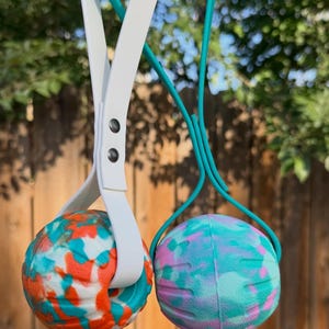 May include: Two spherical toys suspended by long handles. The left toy features a white, orange, and teal marbled pattern held by a white handle. The right toy has a teal, pink, and light blue marbled pattern held by a teal handle.