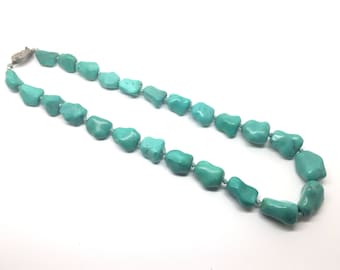 May include: A turquoise gemstone necklace with a silver clasp. The necklace is made of irregular shaped turquoise stones.