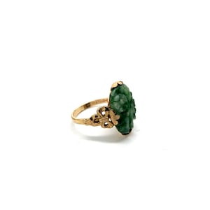 May include: A gold ring with a carved green jade stone. The stone is shaped like a flower and has intricate details.