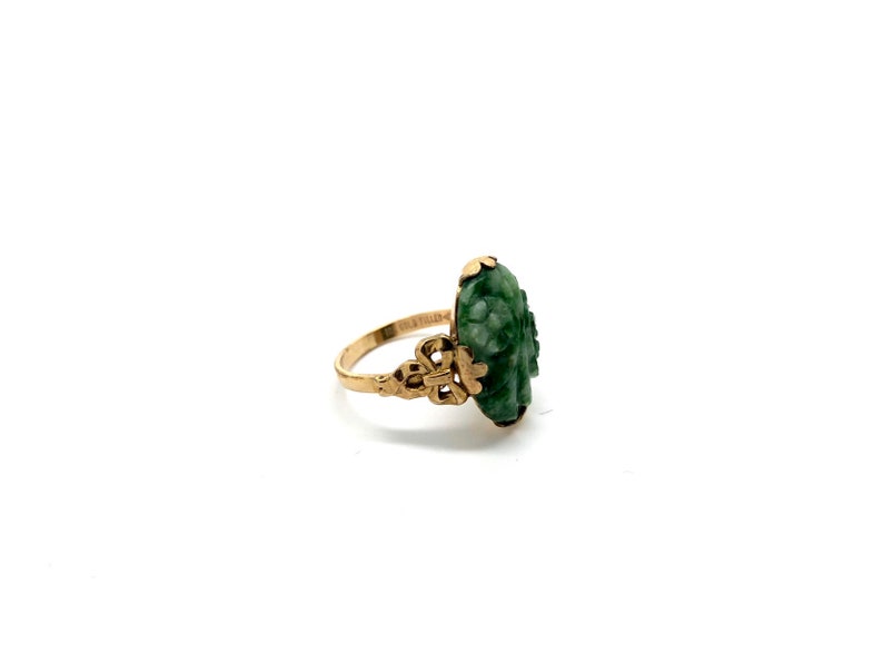 May include: A gold ring with a carved green jade stone. The stone is shaped like a flower and has intricate details.