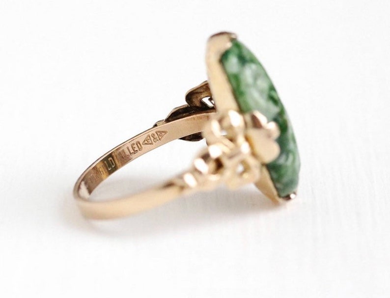 May include: A gold ring with a green jade stone set in a floral design. The ring is marked "10K Filled".