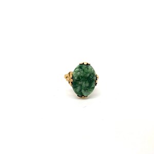 May include: A green jade ring with a gold setting. The jade is carved with a floral design.