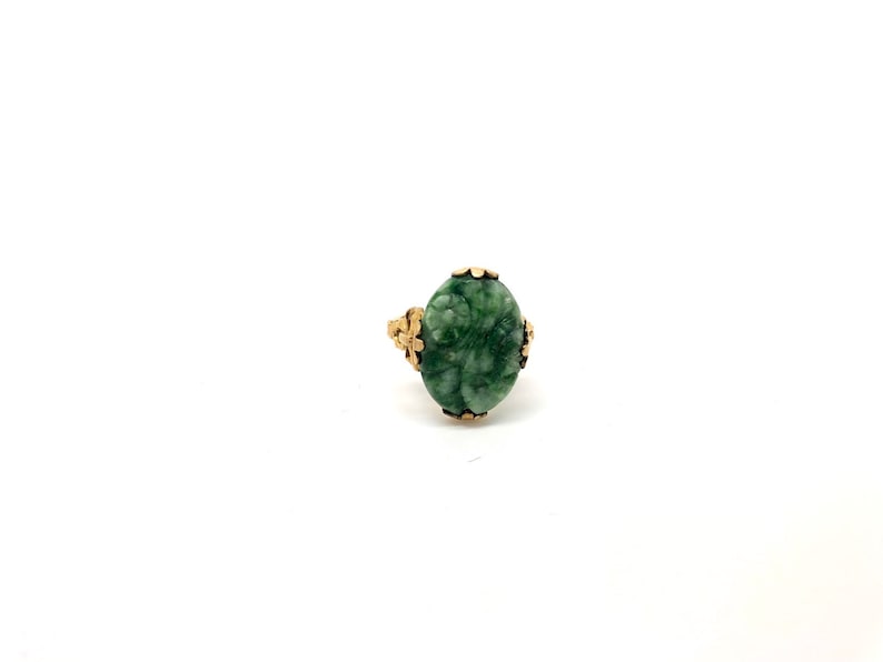 May include: A green jade ring with a gold setting. The jade is carved with a floral design.