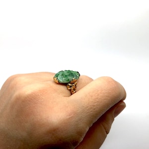 May include: A gold ring with a green jade stone. The stone is carved with a floral design.