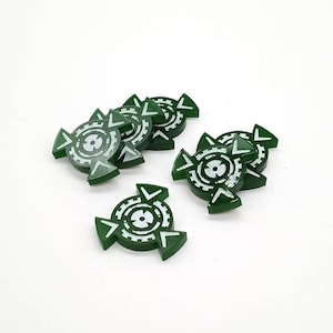 May include: A collection of six small, circular green game tokens featuring a white printed design of a central circle surrounded by a gear-like pattern and three outward-pointing arrowheads. Each token has a smooth, flat surface finish.