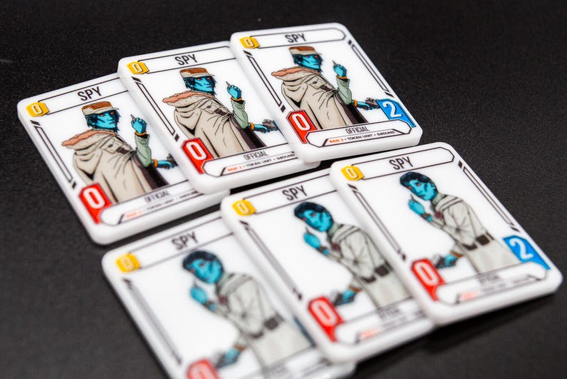 K&ouml;nnte beinhalten: Eine Sammlung wei&szlig;er Spielkarten mit einer Illustration eines blauh&auml;utigen Charakters. Jede Karte tr&auml;gt die Aufschrift "SPY" und eine Zahl, wobei einige "0" und andere "2" zeigen. Die Karten sind auf einer dunklen Oberfl&auml;che angeordnet.