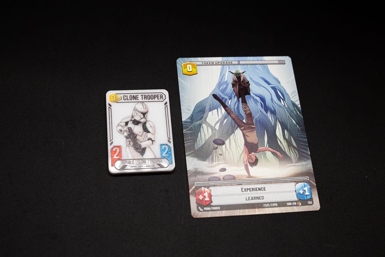 K&ouml;nnte beinhalten: Zwei Star Wars-Spielkarten auf schwarzem Untergrund. Eine Karte zeigt eine Clone Trooper-Illustration, die andere eine Szene mit Yoda und einer Person, die einen Handstand macht. Die Karten haben Text und Spielstatistiken.