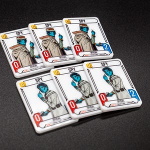 K&ouml;nnte beinhalten: Sechs wei&szlig;e Spielkarten zeigen einen blauh&auml;utigen Charakter in einem beigen Mantel und Hut. Jede Karte tr&auml;gt das Wort "SPY" und eine Zahl in einem roten oder blauen Feld. Die Karten sind auf einer dunklen Oberfl&auml;che angeordnet.