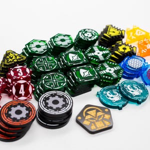 Puede incluir: Una colección de fichas de juego coloridas en varias formas, incluyendo triángulos, hexágonos y círculos. Las fichas son en tonos de verde, rojo, amarillo, naranja y azul. Algunas fichas tienen números, otras diseños geométricos.