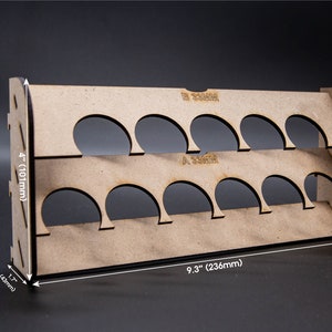 Puede incluir: Un estante de pintura de madera con 12 ranuras para guardar botellas de pintura. El estante mide 101 mm de alto, 236 mm de ancho y 43 mm de profundidad.