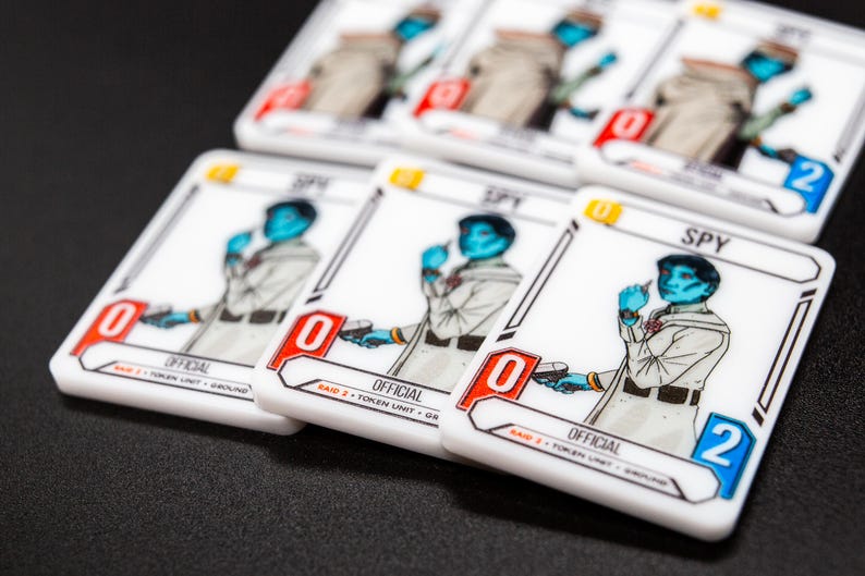 K&ouml;nnte beinhalten: Wei&szlig;e Spielkarten mit einem blauh&auml;utigen Charakter in heller Uniform, beschriftet mit "SPY" und "OFFICIAL". Die Karten haben rote und blaue Akzente, mit einer Null oder Zwei in der Ecke. Die Karten liegen auf einer schwarzen Oberfl&auml;che.