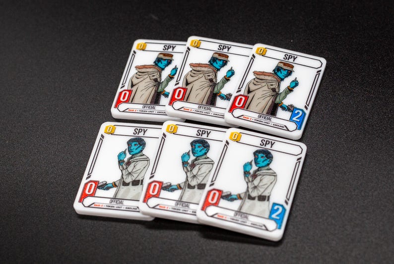 K&ouml;nnte beinhalten: Sechs wei&szlig;e Spielkarten mit einer Illustration eines blauh&auml;utigen Charakters, beschriftet mit "SPY". Die Karten haben eine rote oder blaue Nummer, und die Nummer "0" befindet sich auf den meisten Karten. Die Karten liegen auf einer schwarzen Oberfl&auml;che.