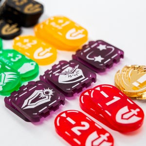 Puede incluir: Una colección de fichas y dados de juego coloridos. Las fichas tienen varias formas y colores, incluyendo verde, amarillo, morado, rojo y dorado. Algunas fichas tienen símbolos y texto blancos, como "+3 Assault" y números.