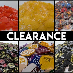 Könnte beinhalten: Eine Sammlung von Spielmarken in verschiedenen Farben, darunter Rot, Gelb, Schwarz und Lila. Die Marken weisen unterschiedliche Designs und Formen auf, mit dem Wort "CLEARANCE" in großen weißen Buchstaben über dem Bild. Diese Marken sind wahrscheinlich für Brett- oder Tischspiele.