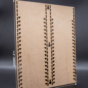 Puede incluir: Una tabla de madera marrón con dos filas de agujeros espaciados uniformemente a lo largo de los bordes. La tabla mide 23,6 cm por 30 cm.