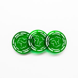 May include: Three green, circular tokens with a white cloud design in the center. Each token has a white, dotted border. The tokens are arranged in a row against a white background. These tokens could be used for a board game.