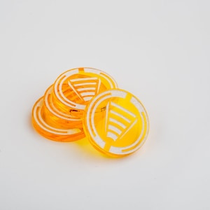 Op de afbeelding: Een stapel van vijf gele plastic tokens met een wit symbool van een driehoek met lijnen in een cirkel.