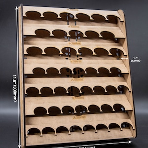 Puede incluir: Un organizador de botellas de pintura de madera con múltiples estantes. El organizador mide 300 mm de alto, 236 mm de ancho y 43 mm de profundidad. Cada estante tiene varios recortes circulares para sostener botellas. El texto "A 20MM" es visible.