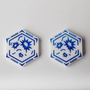 May include: Two white hexagonal tiles with a blue geometric design. The design features a central starburst with smaller stars and lines.