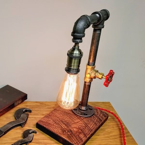 May include: A black pipe lamp with a red valve and a wooden base. The lamp is lit with a vintage-style light bulb.