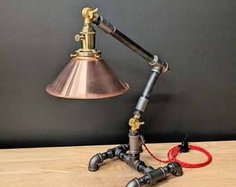 May include: A black and copper industrial style table lamp with a copper shade and a black pipe base. The lamp has a red cord and a black plug.